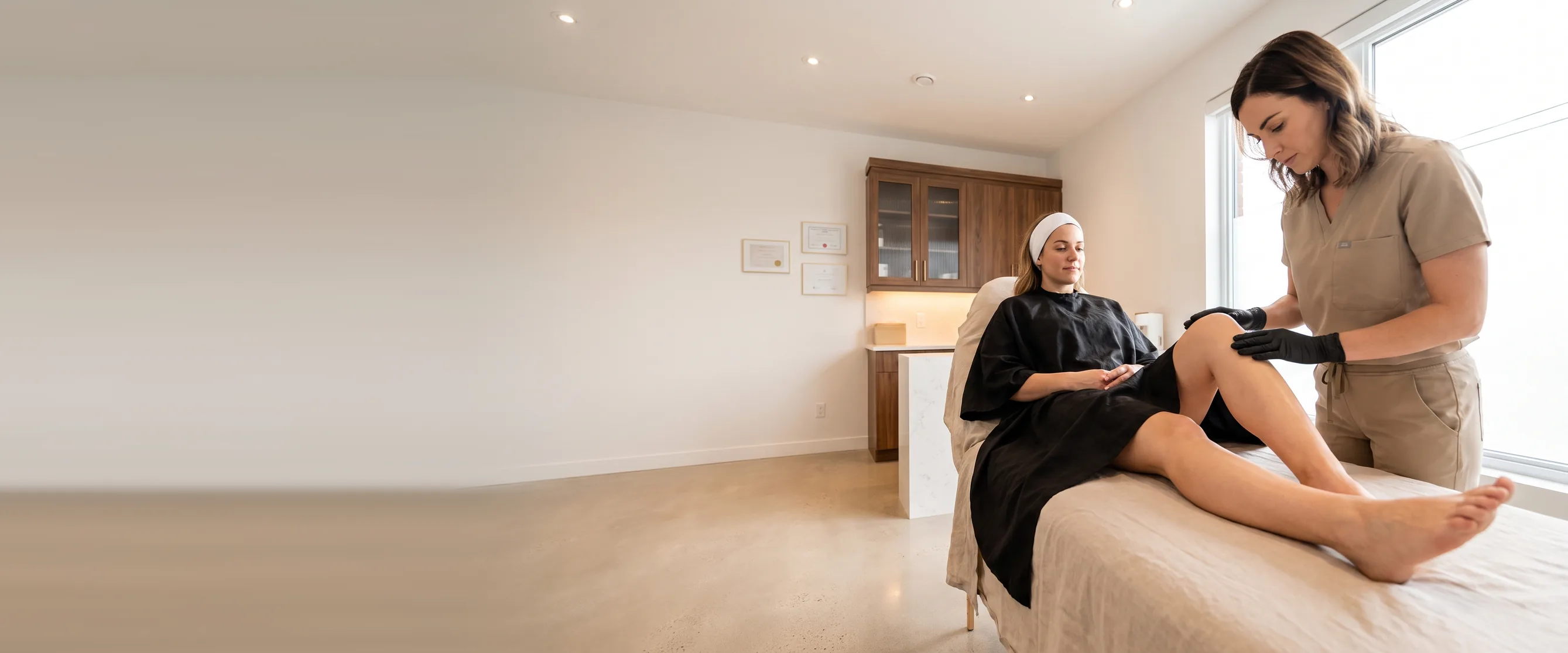 An esthetician checks the leg of a client lying on a treatment table at the institute