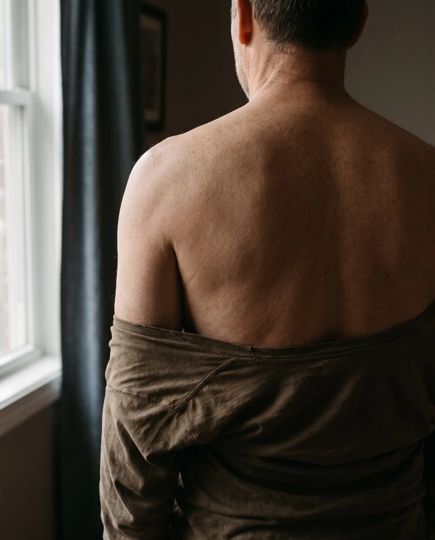 Dos et epaules d'un homme, de dos, pres d'une fenetre