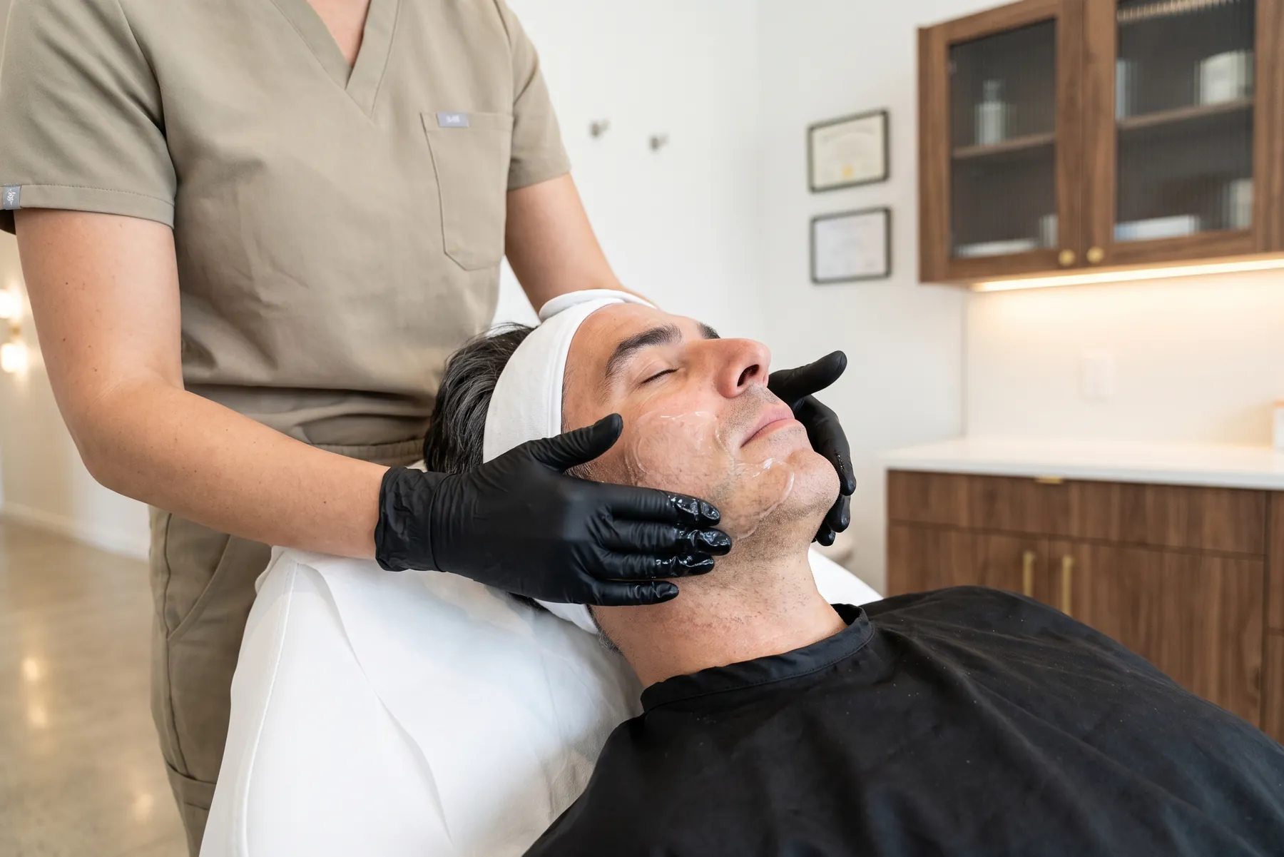 Produit étalé du bout des doigts gantés le long de la mâchoire d'un homme
