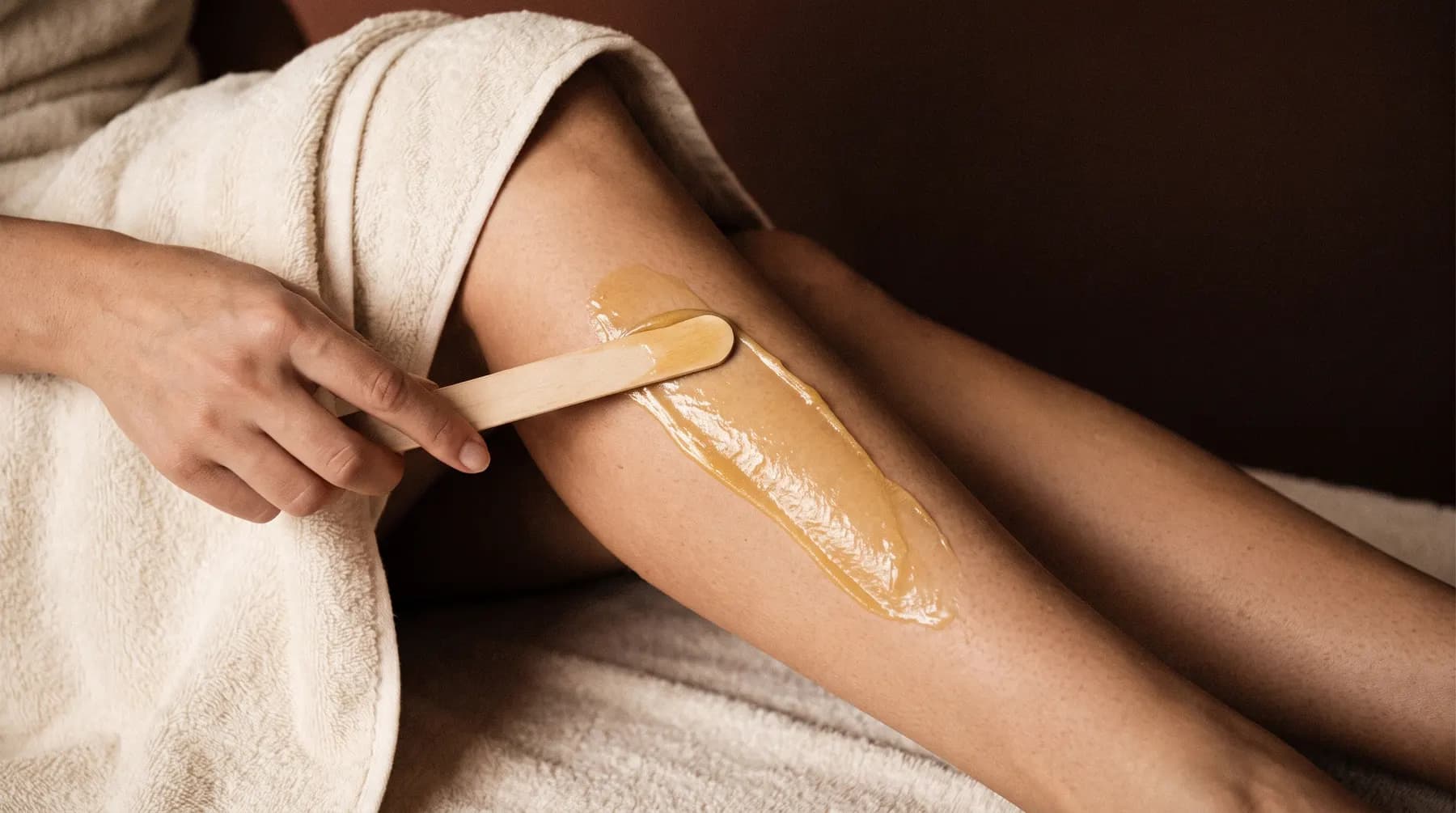 A spatula of warm wax spread on a client's leg, over a cotton towel