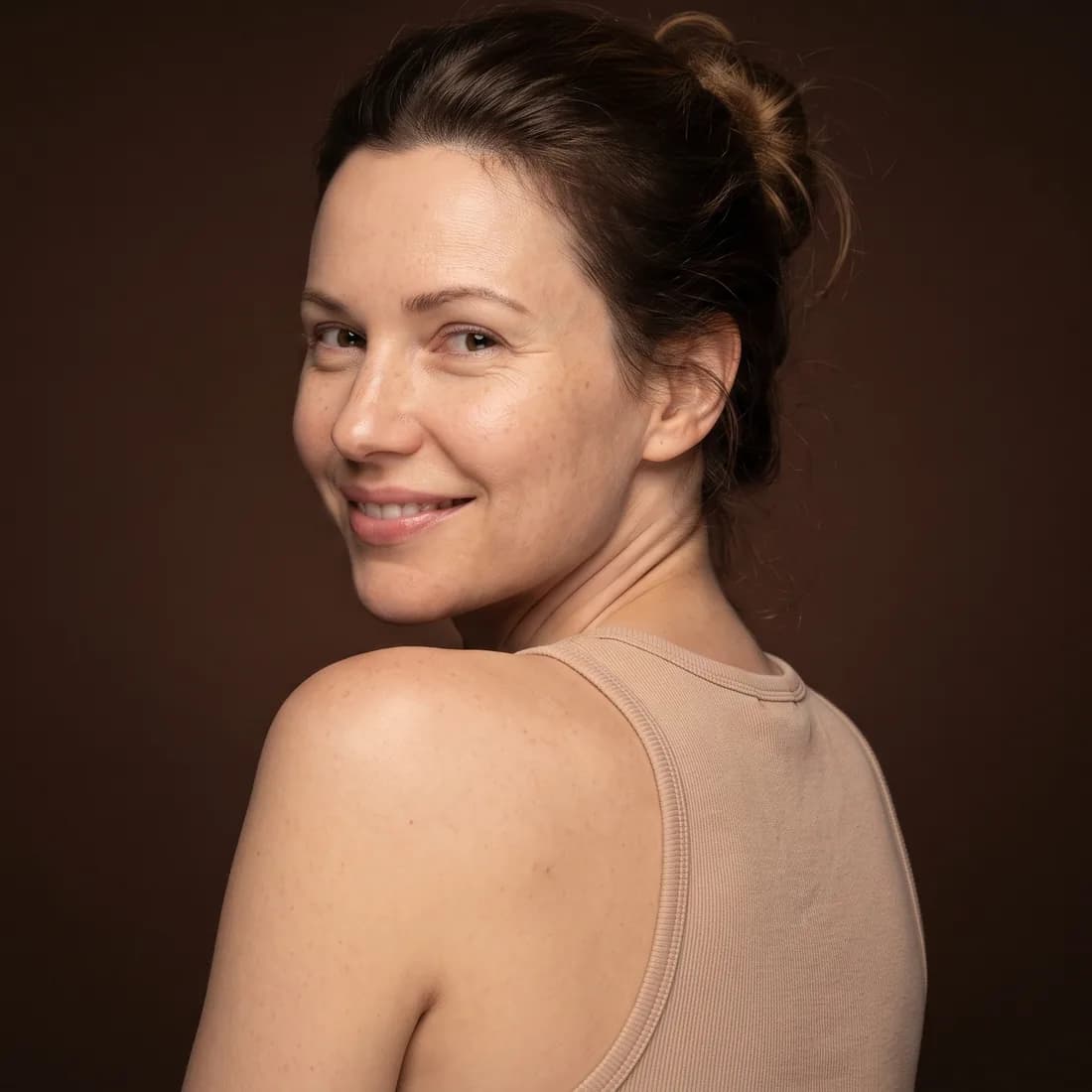 Woman seen from behind, shoulders down, turned toward the camera, peaceful smile