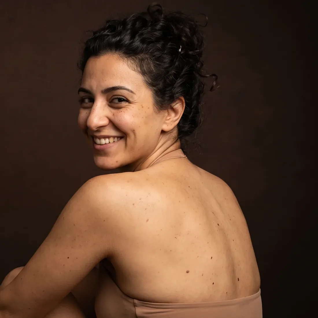 Woman seen from behind, bare shoulders, turned toward the camera with a broad smile