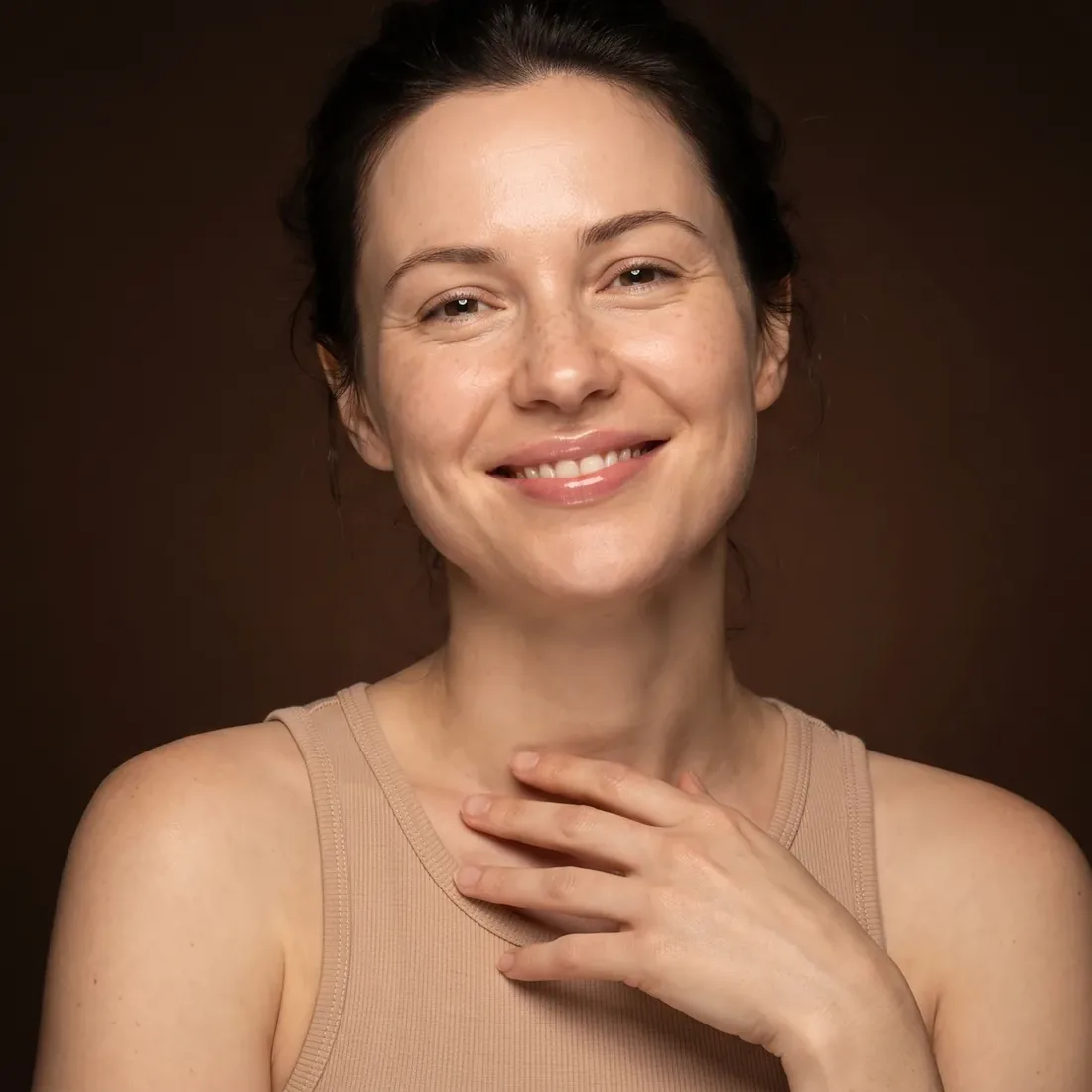 Smiling woman, bare luminous skin, against a deep brown background