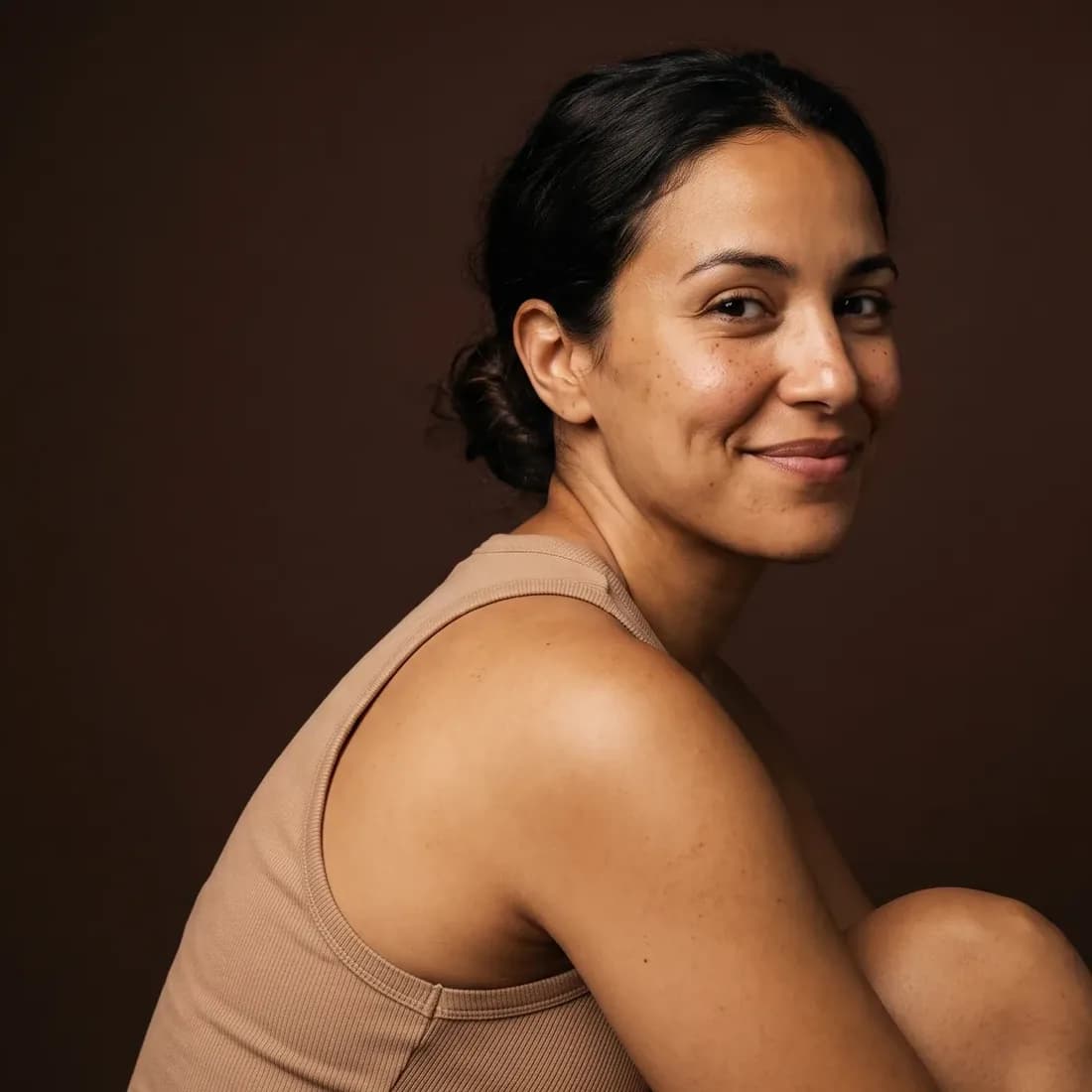A woman turned to the camera over her shoulder, holding back a smile, an even complexion