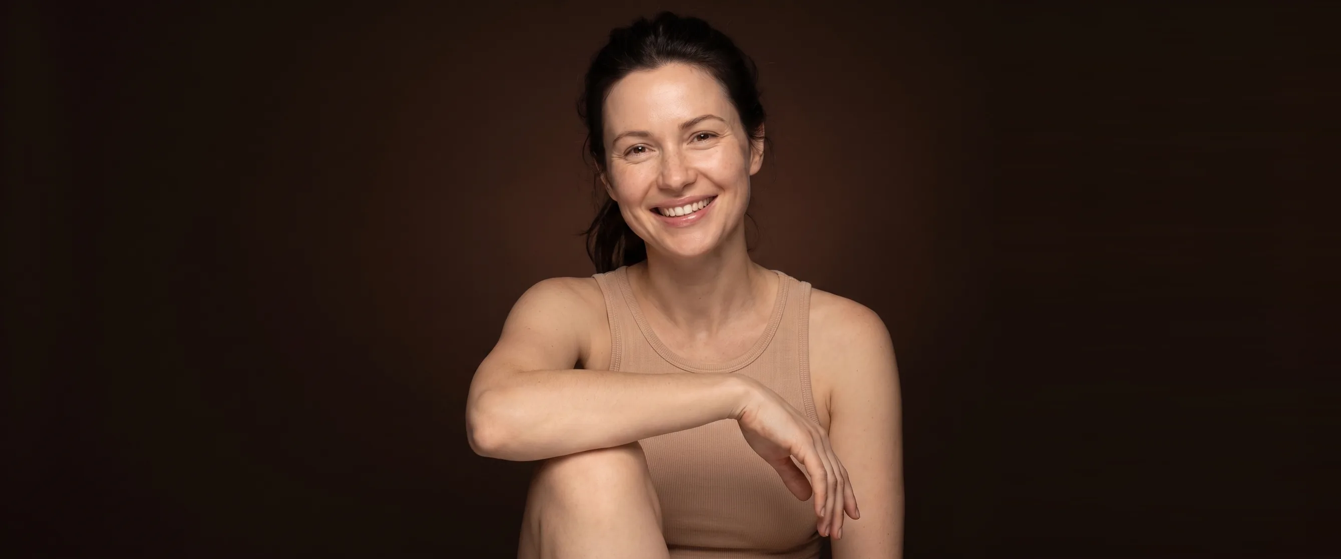 Athletic woman seated, one forearm on her knee, relaxed smile
