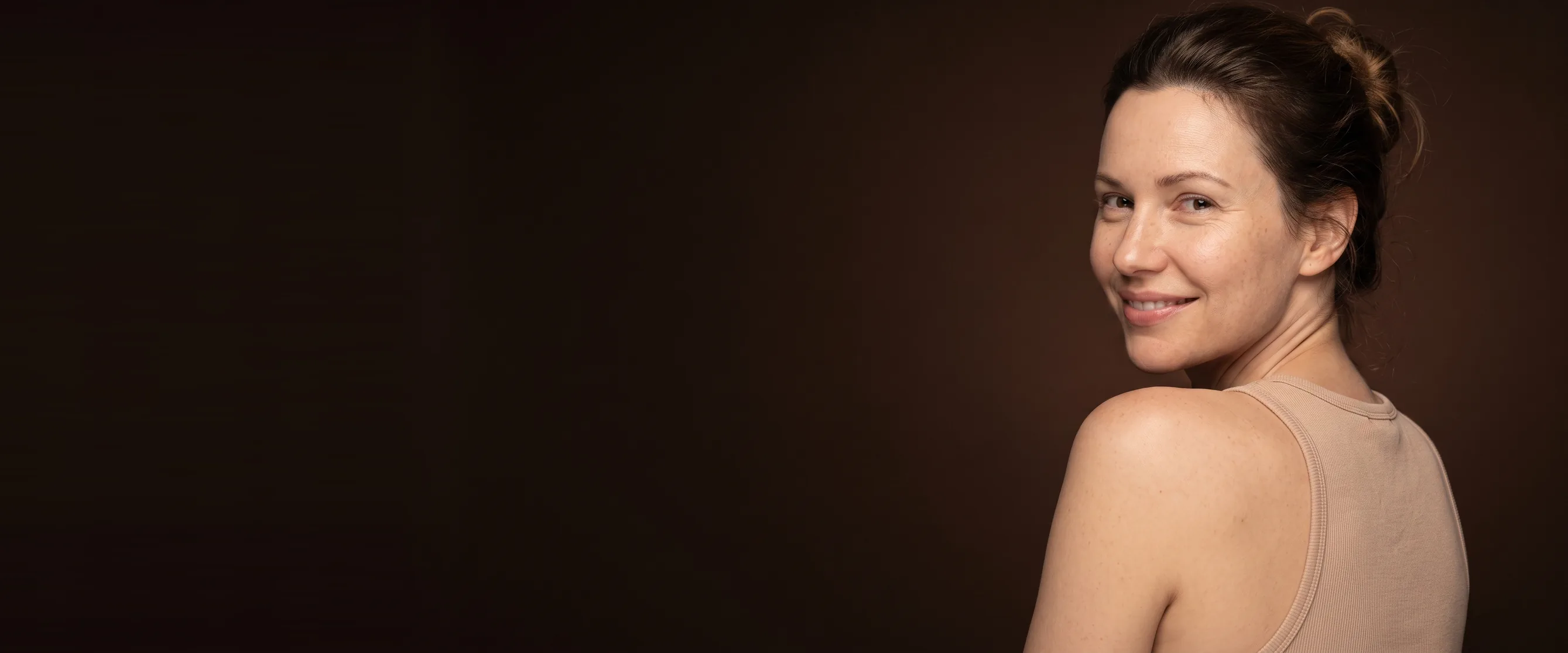 Woman seen from behind, shoulders down, turned toward the camera, peaceful smile