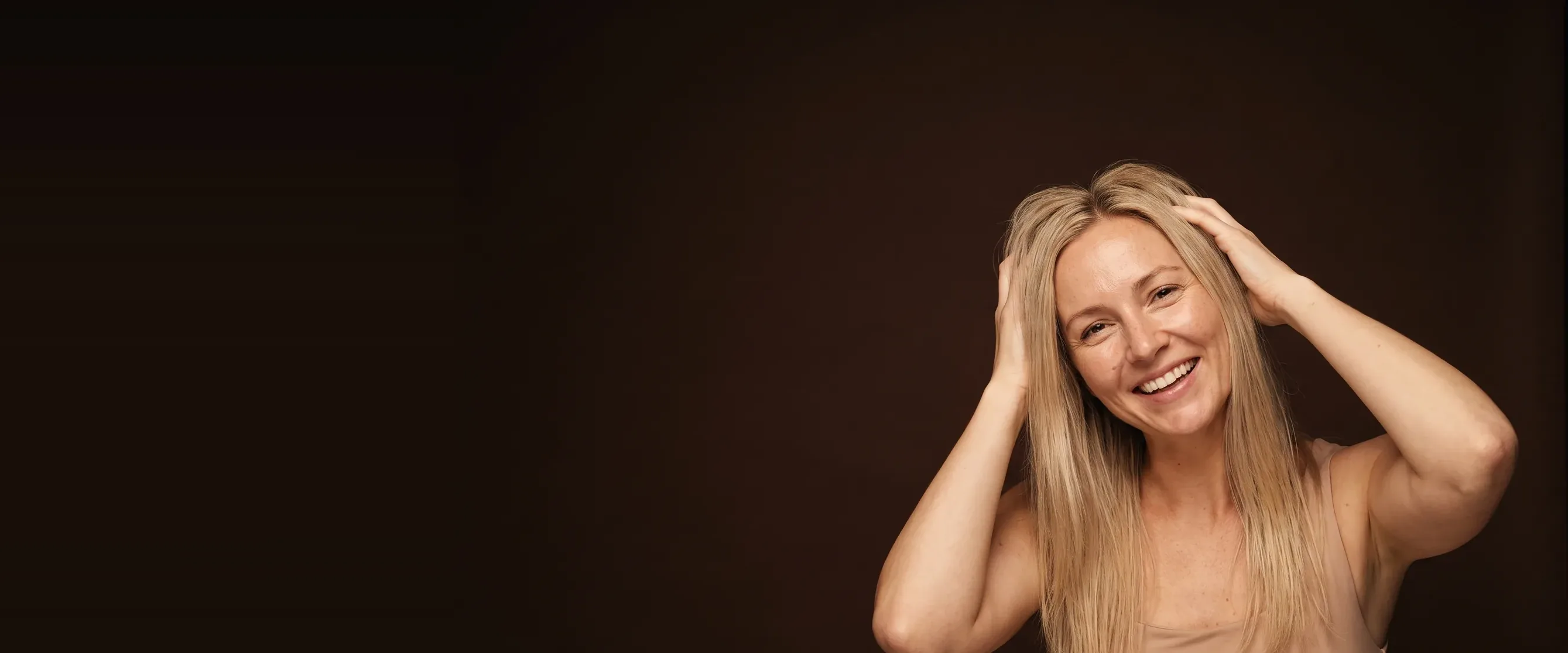 A woman laughing softly, fingers running through her hair at the roots
