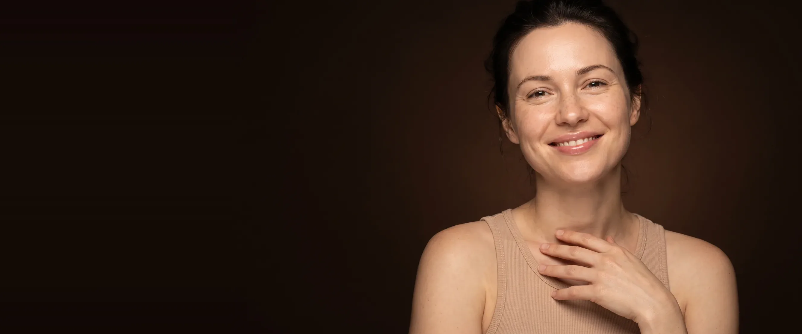 A smiling woman, bare and luminous skin, on a deep brown background