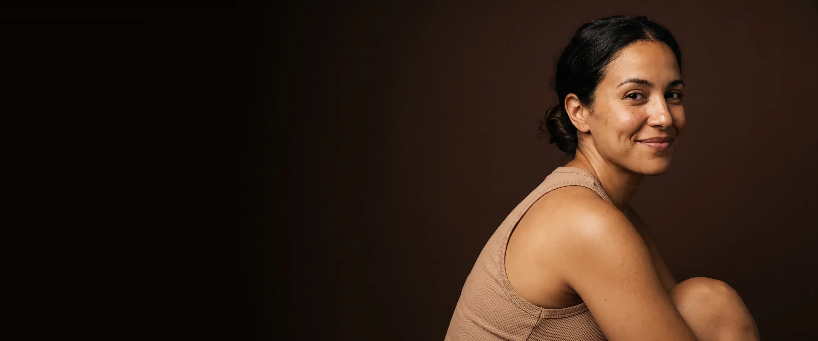 A woman turned to the camera over her shoulder, holding back a smile, an even complexion